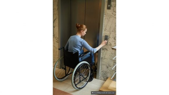 Mujer usuaria de silla de ruedas llamando al ascensor.